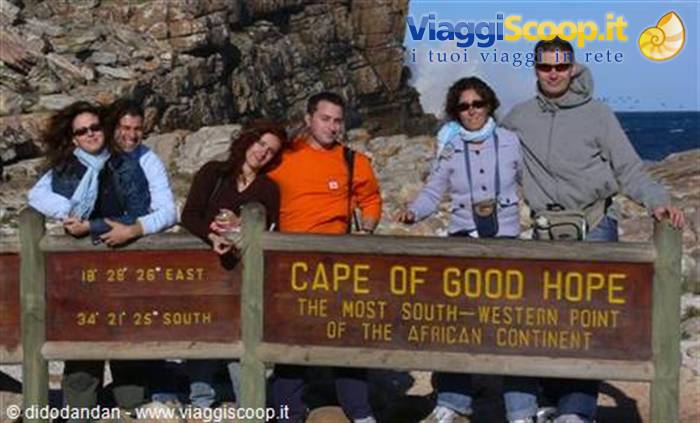 Tourists behind the wooden Cape of Good Hope sign, rocks and ocean