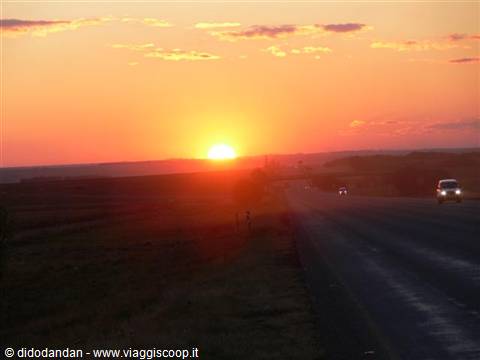 Low sun glowing orange over the highway, cars driving with headlights on
