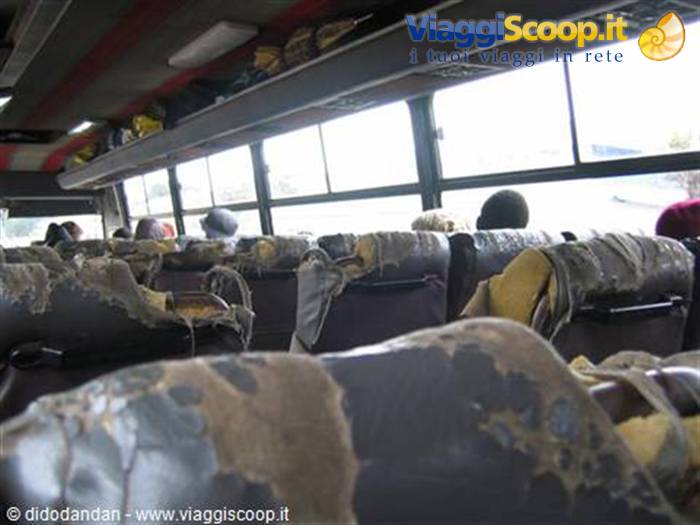 Inside a worn bus with tattered rubber seats and passengers seated