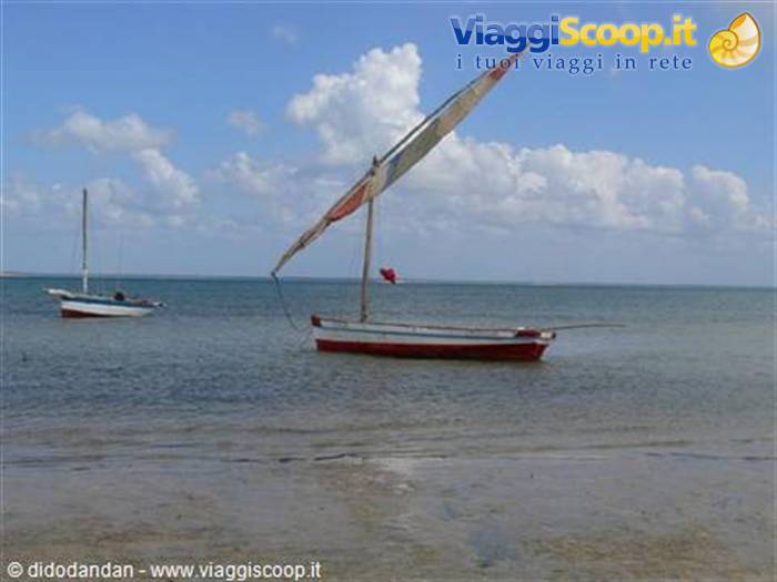 Red and white sailboat anchored near the shore, another boat in the background