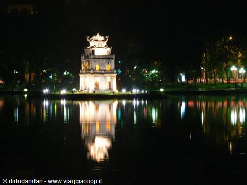 Turtle Tower lit up at night on Hoan Kiem Lake, reflected in the water