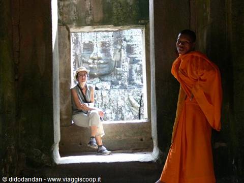 Orange-robed monk beside seated woman, stone faces of Bayon temple