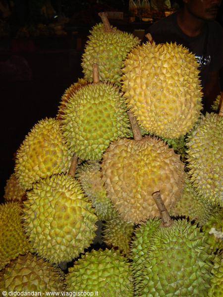 Pile of spiky yellow and green durians stacked at the market, vendor nearby