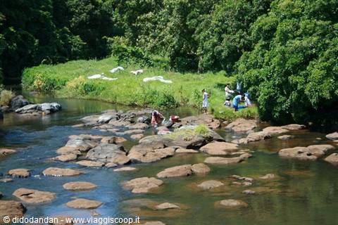 Women washing clothes in a river among red rocks and lush greenery