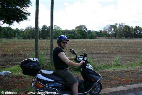 Man in blue helmet sitting on a black scooter by a rural road
