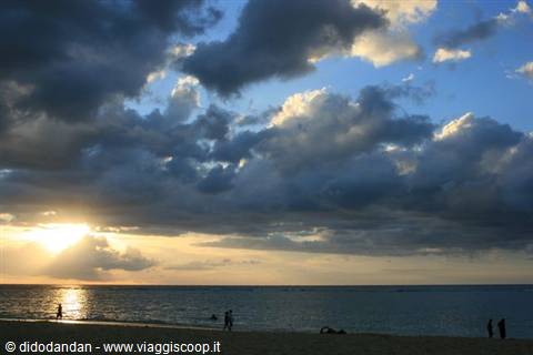 dark clouds over calm sea, people walking on sandy beach