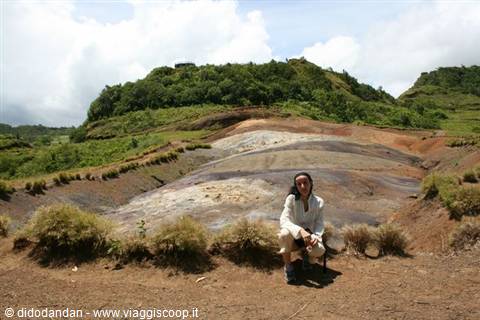 Woman crouching before mineral volcanic ground, green hills and white clouds