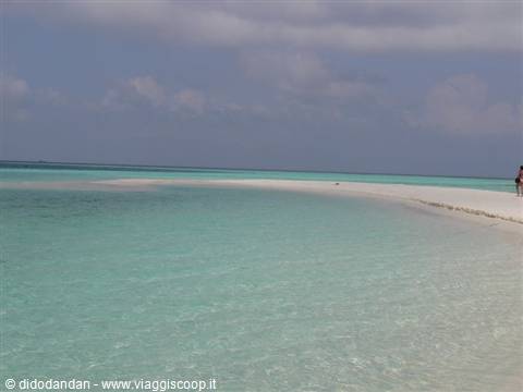 White sand beach with clear turquoise water, tourists walking along the shore