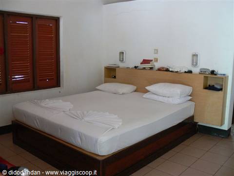 Hotel room with white double bed, wooden headboard and red shutters