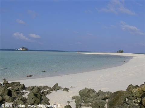 White sand and black rocks before turquoise water with anchored boat