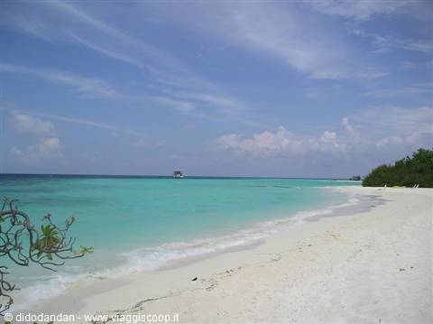 White sand beach with turquoise sea, a boat offshore under cloudy sky