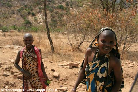 Two smiling Maasai girls among dry trees on arid ground