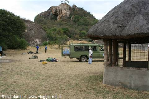 Green safari jeep beside a thatched hut, backpacks on dry grass