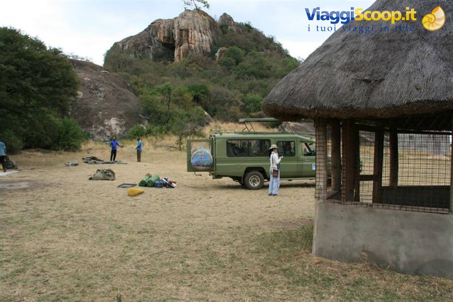 Green safari jeep beside a thatched hut, backpacks on dry grass