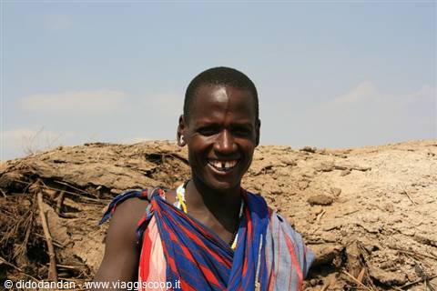 Smiling Maasai woman in red and blue shawl by an earthen wall