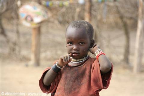 Child wearing colorful bracelets and white beaded necklace in a rural village