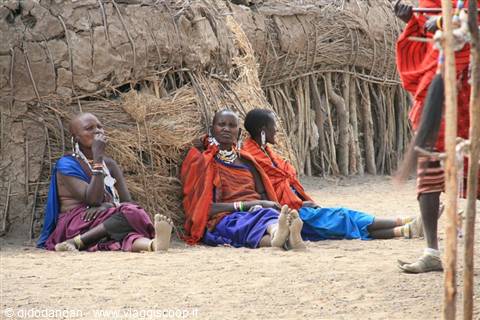 Maasai women sitting near huts made of branches and mud