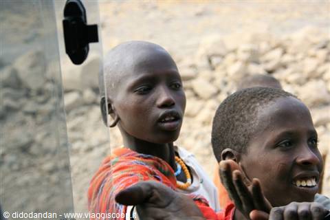 Two Maasai boys with beaded necklaces peer through the safari truck window