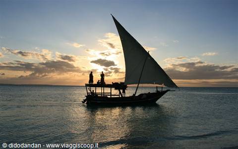 Sail-powered dhow with two fishermen silhouetted on calm water at dusk