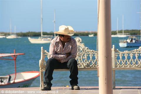 Man in straw hat sitting on wrought iron bench, boats at La Paz