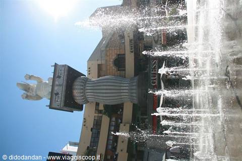 Fountain with water jets in front of Gucci store, white statue atop a column