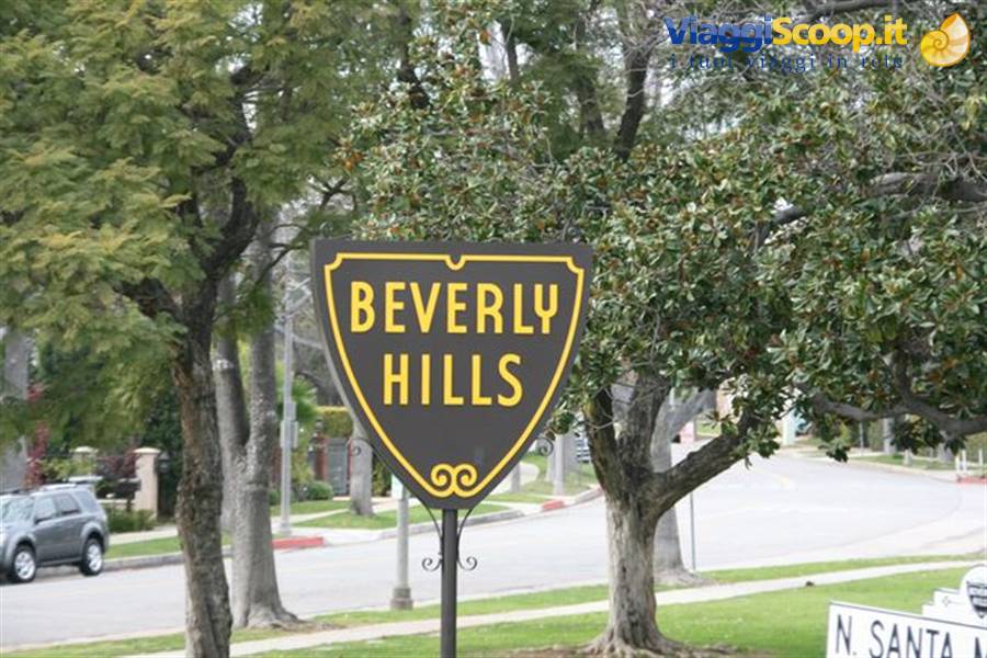 Yellow Beverly Hills shield sign beside a tree-lined street, cars parked under trees