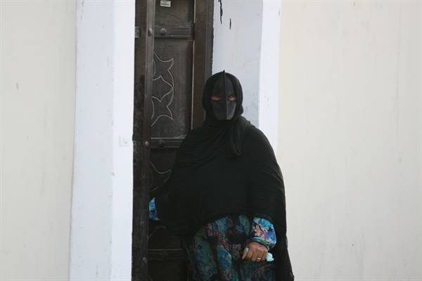 Woman in black veil beside a carved wooden door, white plastered walls