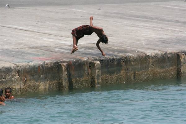 Boy backflipping off the concrete pier, others swimming in the green water