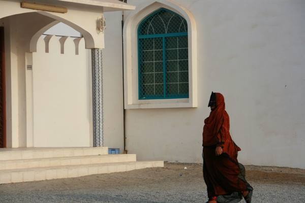 Woman in red veil walks past white building with green window