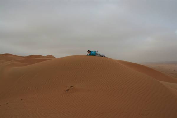 Woman lying on an orange sand dune under a grey overcast sky