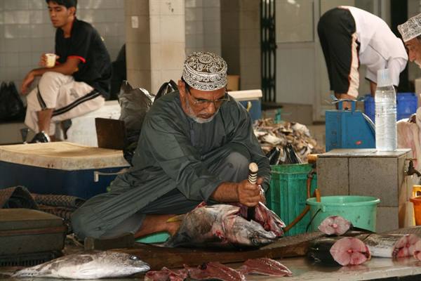 Fishmonger in embroidered cap cutting a large tuna at the fish market