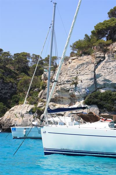 White sailboats anchored in rocky cove with turquoise water