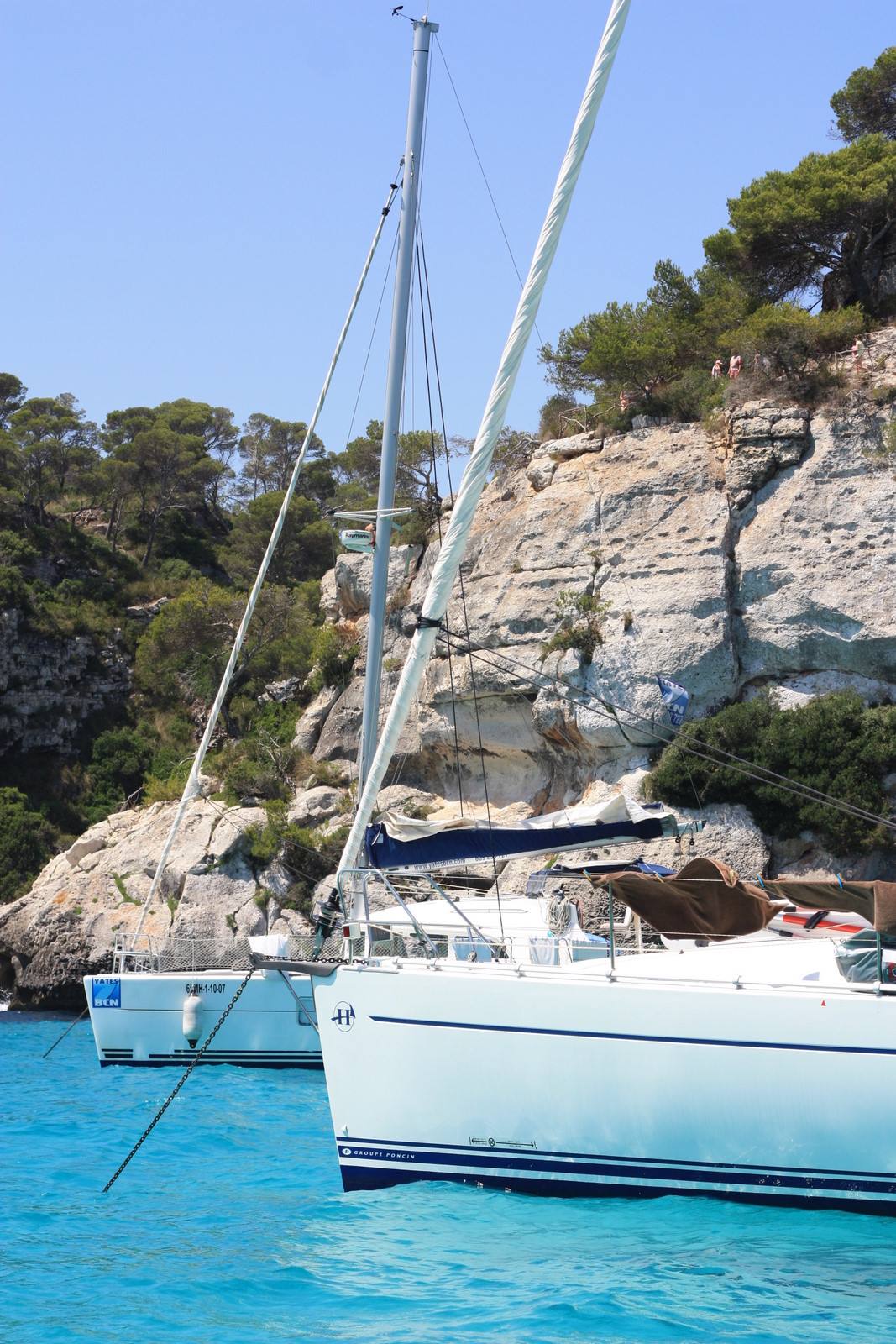 White sailboats anchored in rocky cove with turquoise water