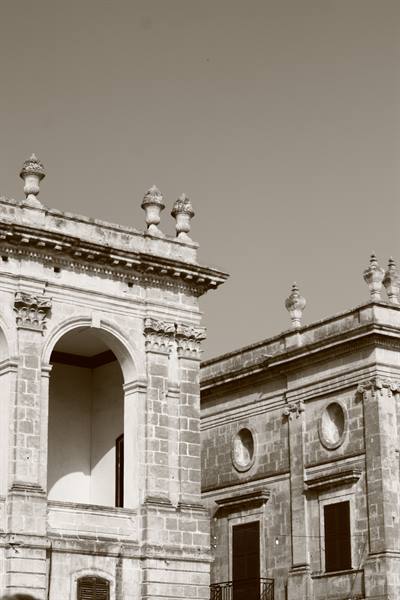 Baroque stone facades with arches, statues and strong sunlight