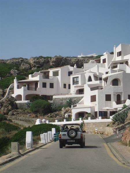 Jeep on the road in front of whitewashed Mediterranean houses on green rock