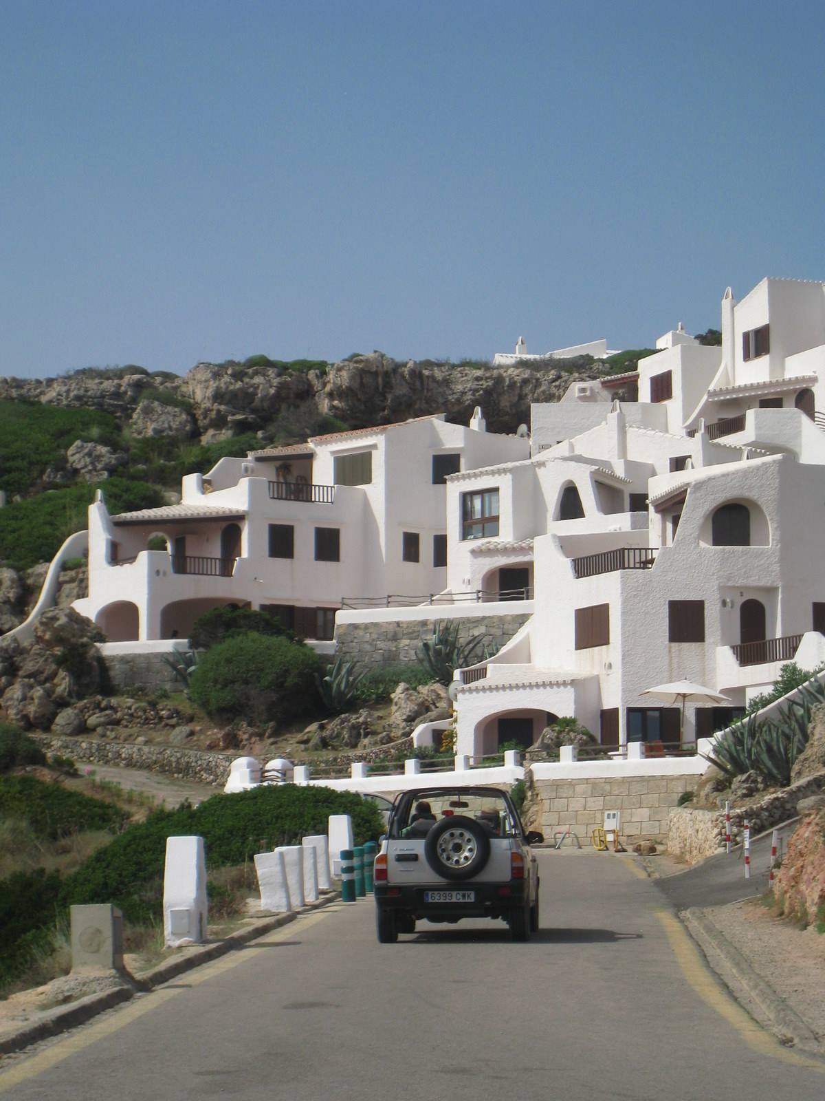 Jeep on the road in front of whitewashed Mediterranean houses on green rock