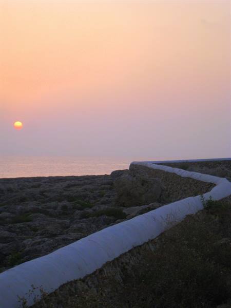 Whitewashed stone wall over the rocks, low sun on the sea