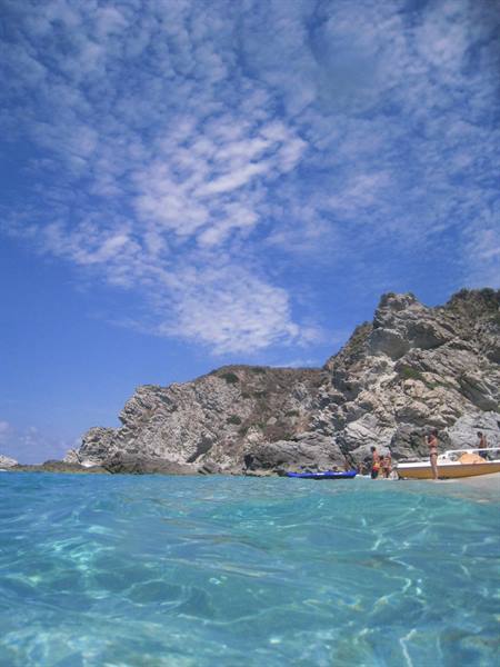 Turquoise water and granite rocks with boats, swimmers under a cloudy sky