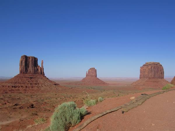 Monument Valley: red sandstone buttes under blue sky, sand and shrubs