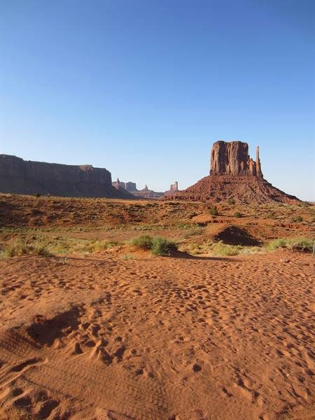 Footprints in red sand before Monument Valley mittens in morning light