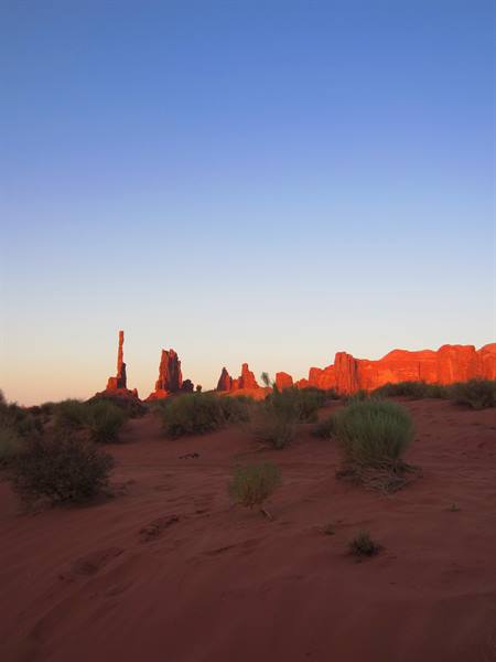 Monument Valley, red rock spires glowing in early sun above desert shrubs