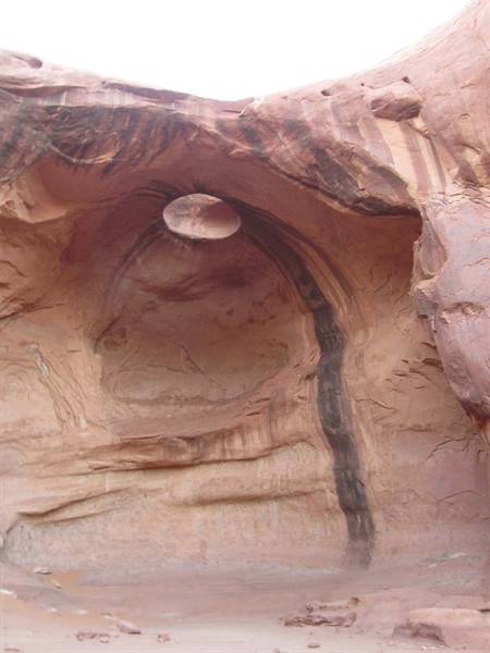 Round hole in red sandstone cliff, daylight shining through the rock arch