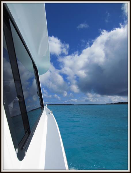 White boat bow on turquoise water, clouds over a distant strip of land