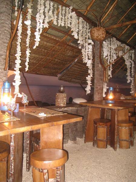 Wooden beach bar with oil lamps and shells hanging from thatched roof