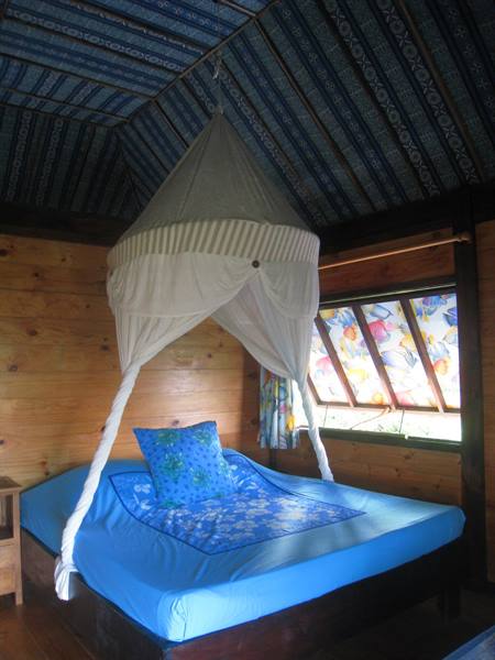 Blue bed with white mosquito net in wooden bungalow, decorated blue ceiling