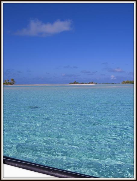 Clear turquoise water from a boat, palm islets on the horizon