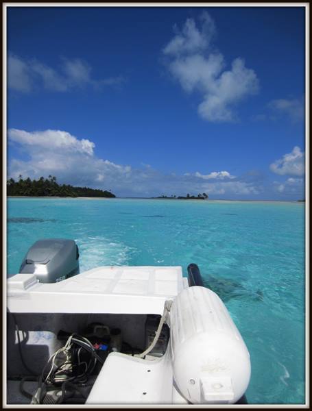 White inflatable boat with outboard motor in turquoise lagoon near a motu