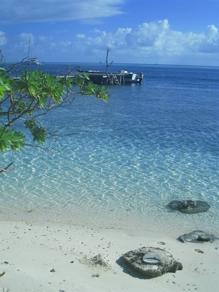 White sand beach, clear turquoise water, boat moored at wooden pier