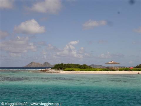 tropical beach with turquoise water, wooden gazebo and hills on the horizon