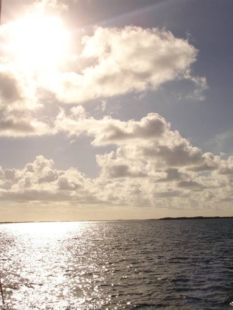 Sun among clouds over the sea with shimmering reflections and distant shore